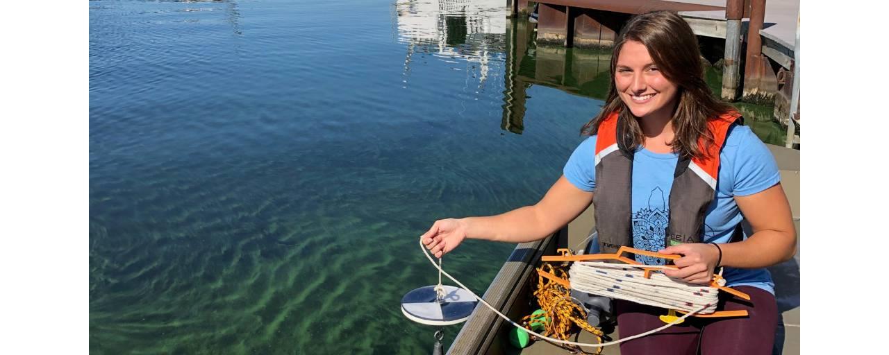 Jasmine Mancuso holds a secchi disk over a Muskegon Lake cyanobacterial bloom